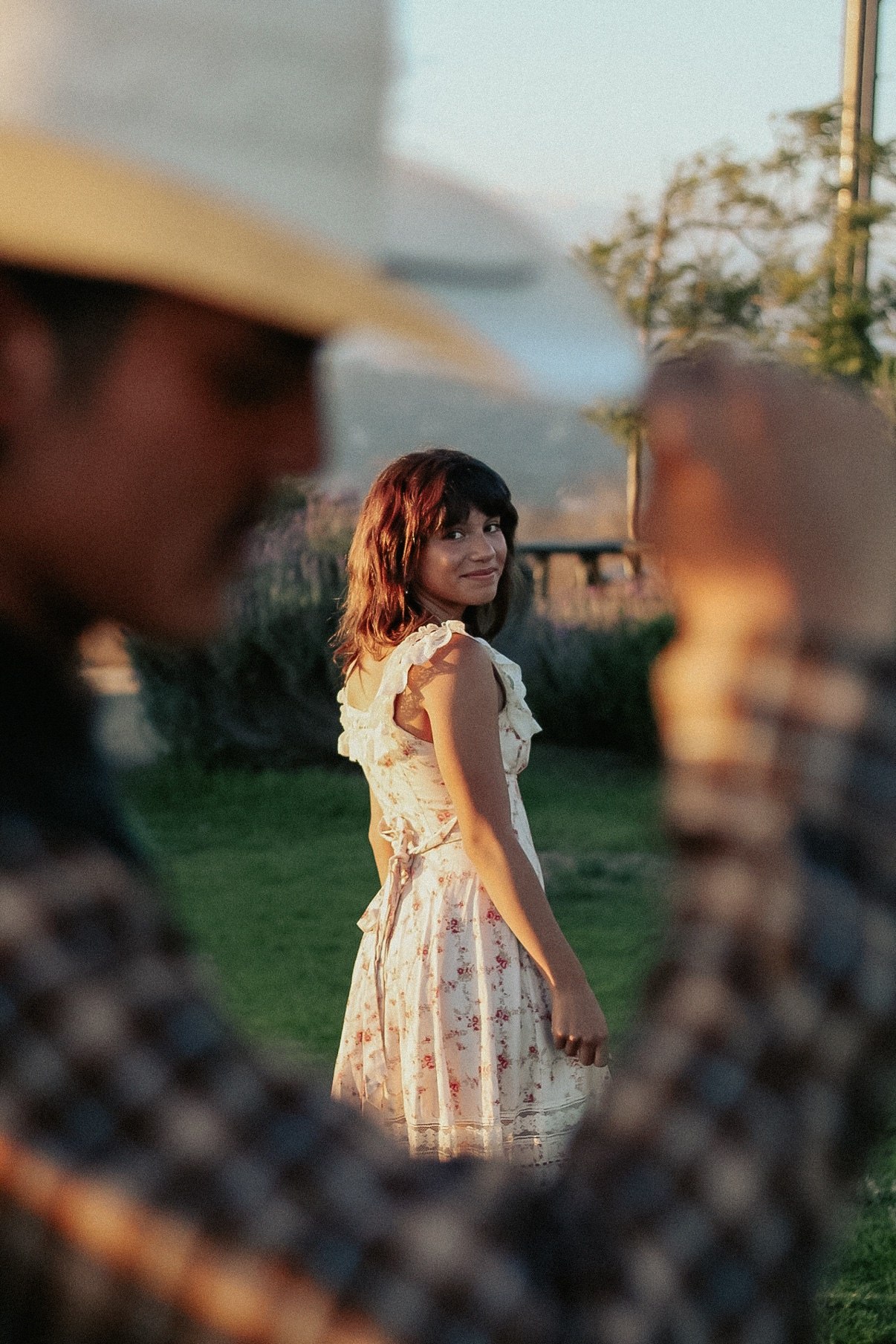 Young woman in a floral dress glancing back over her shoulder in golden-hour light