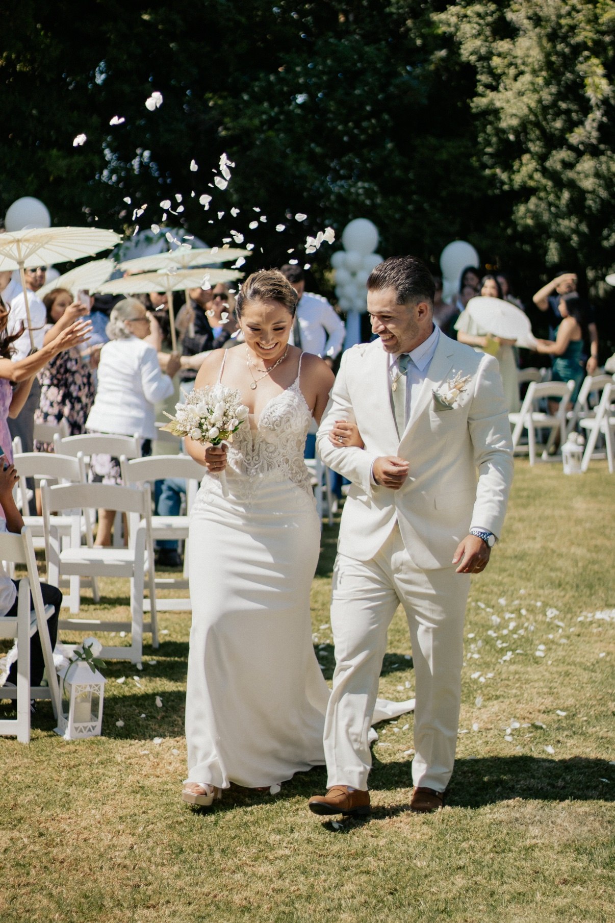 Bride and groom walking arm in arm back down the aisle as guests toss white petals
