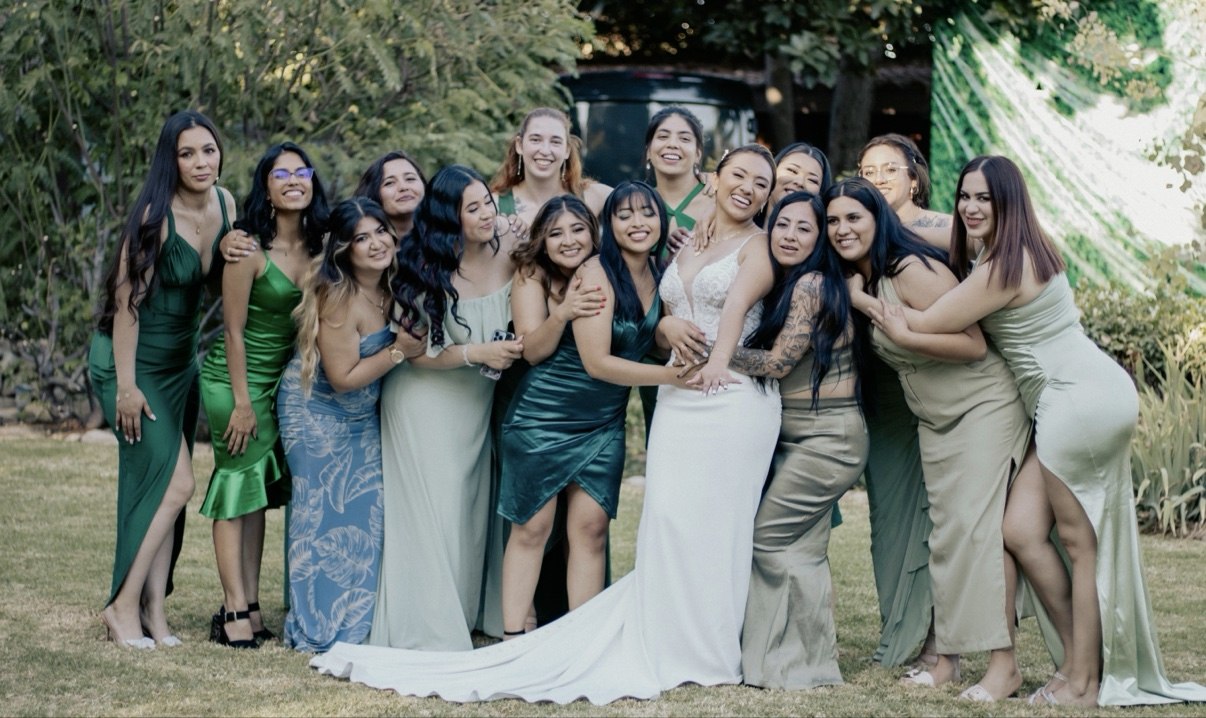 Bride in a white gown laughing with her bridesmaids in green and sage dresses on the lawn