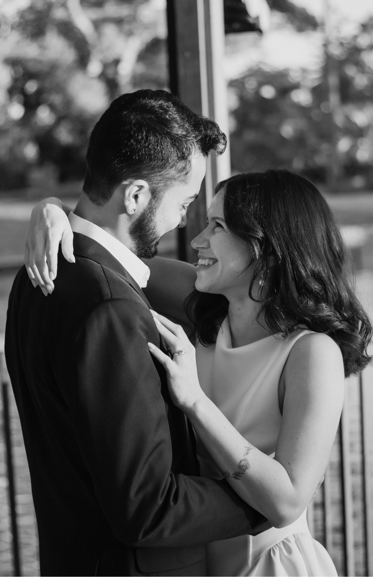 Black-and-white photo of a couple embracing and smiling at each other, her engagement ring visible on his chest