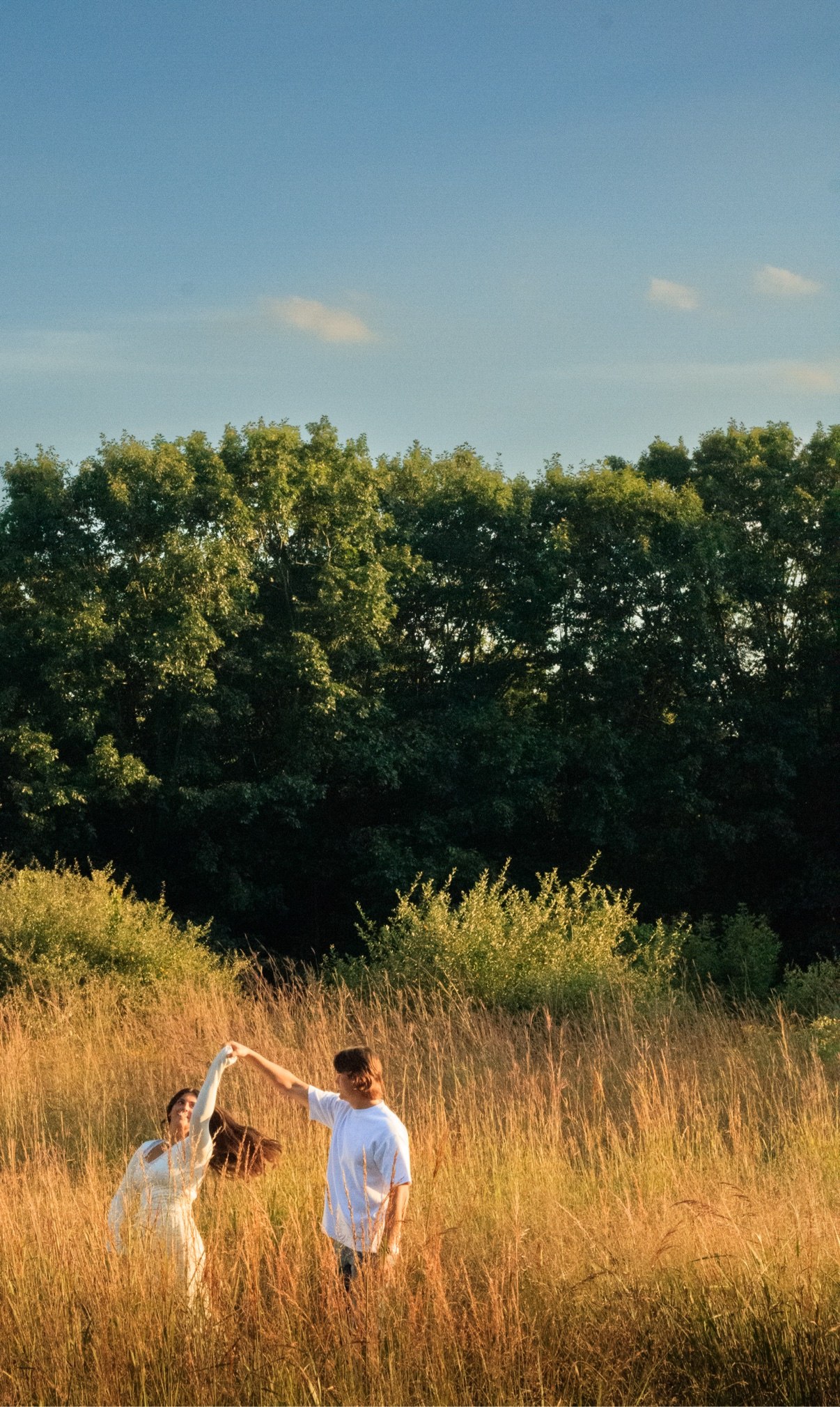 Man twirling his partner in a white dress in a tall golden field under a blue sky