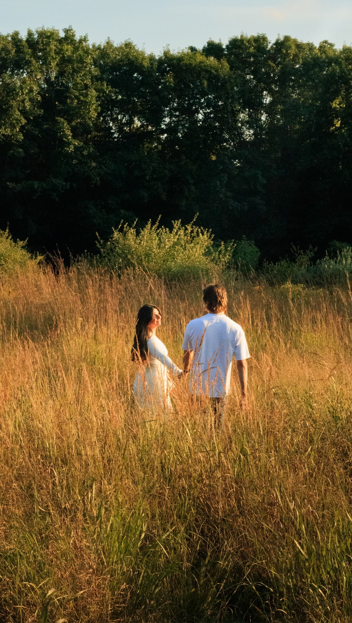 Couple holding hands and walking away through tall golden grass toward the trees
